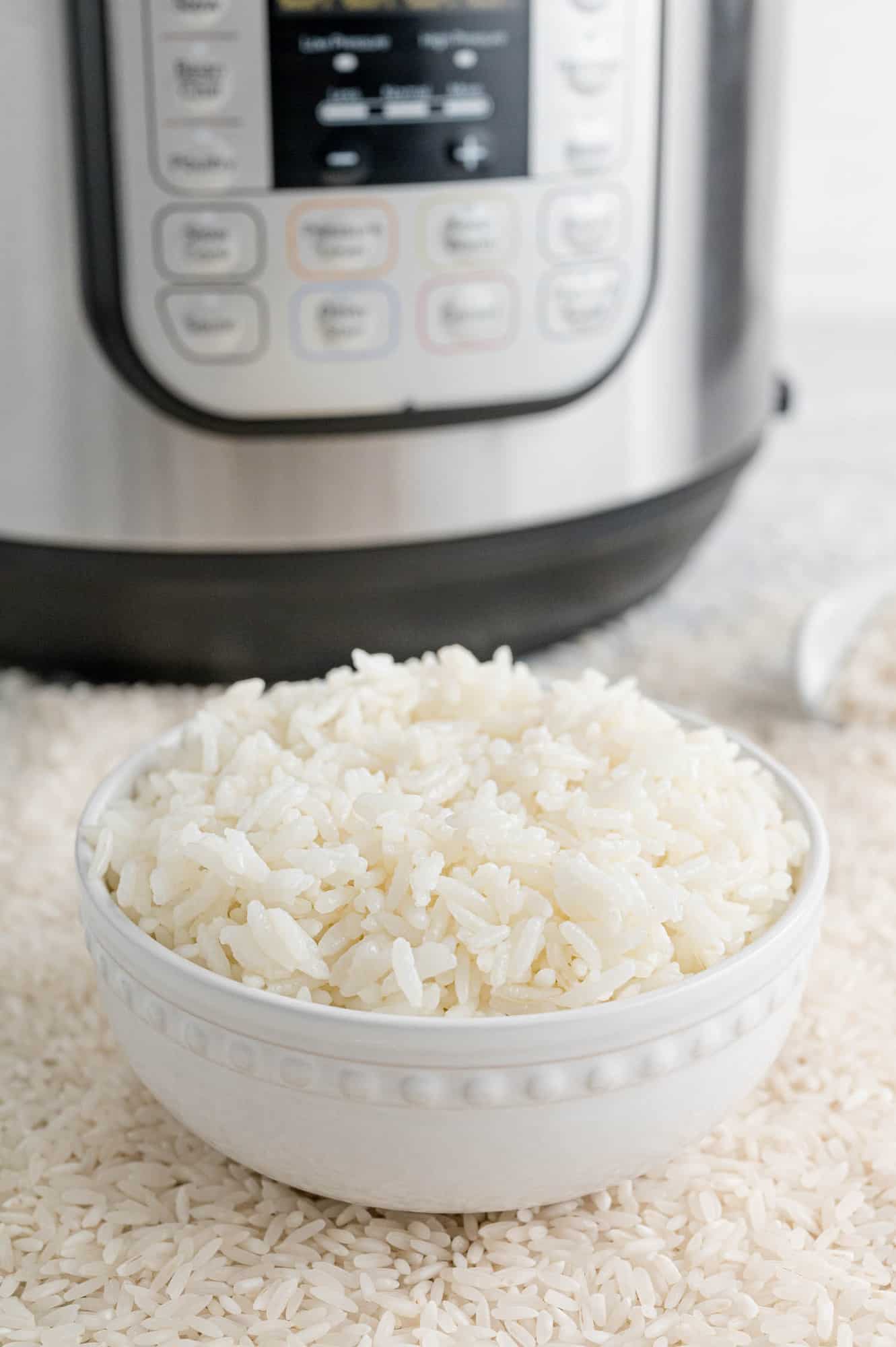 Rice in a bowl in front of a pressure cooker.