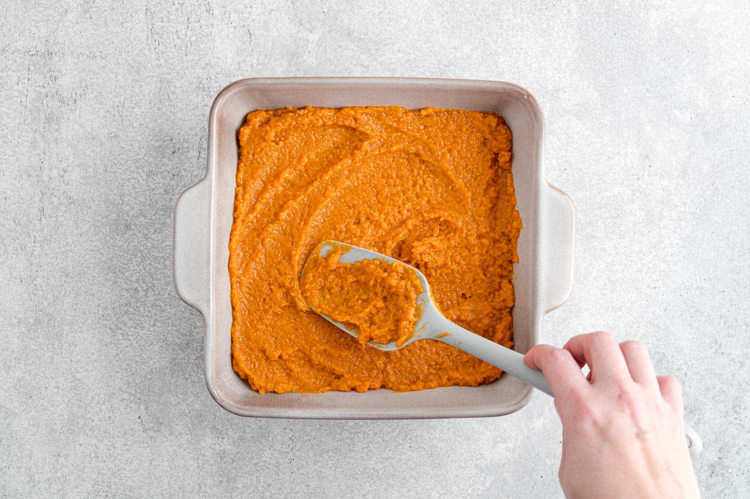 Sweet potatoes being spread into baking dish.