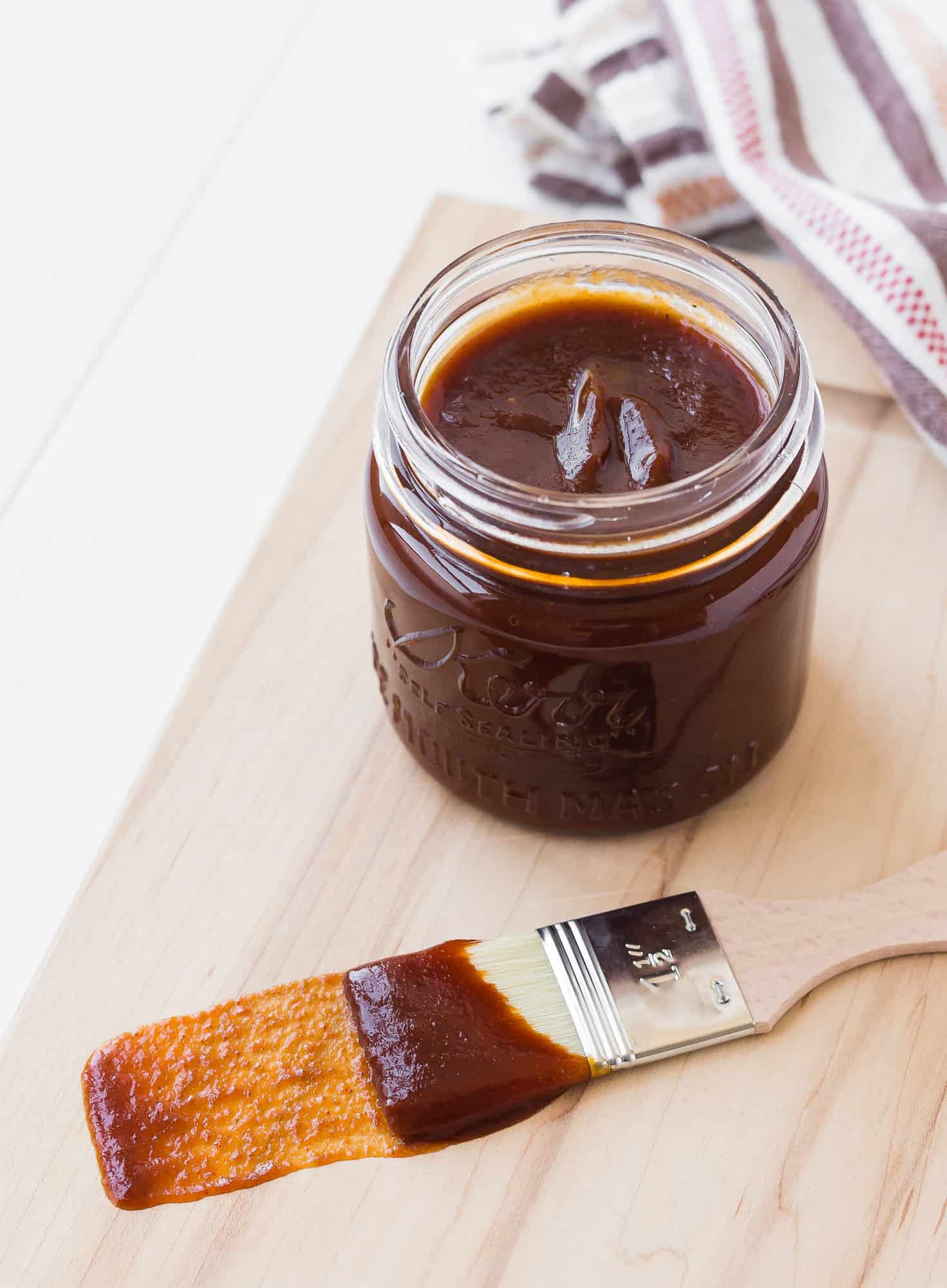 Barbecue sauce in a small glass jar and on a wooden handled brush.