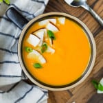 Overhead view of bright orange carrot soup with coconut and green onion garnish.