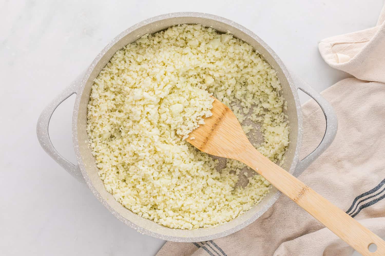 Cooked cauliflower rice in a white skillet.