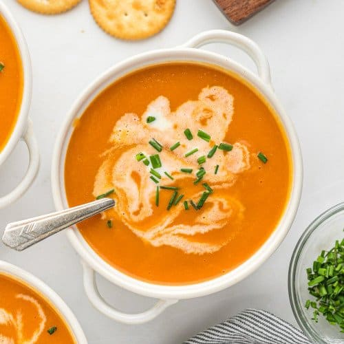 Carrot soup in a white bowl topped with chives and a swirl of cream.