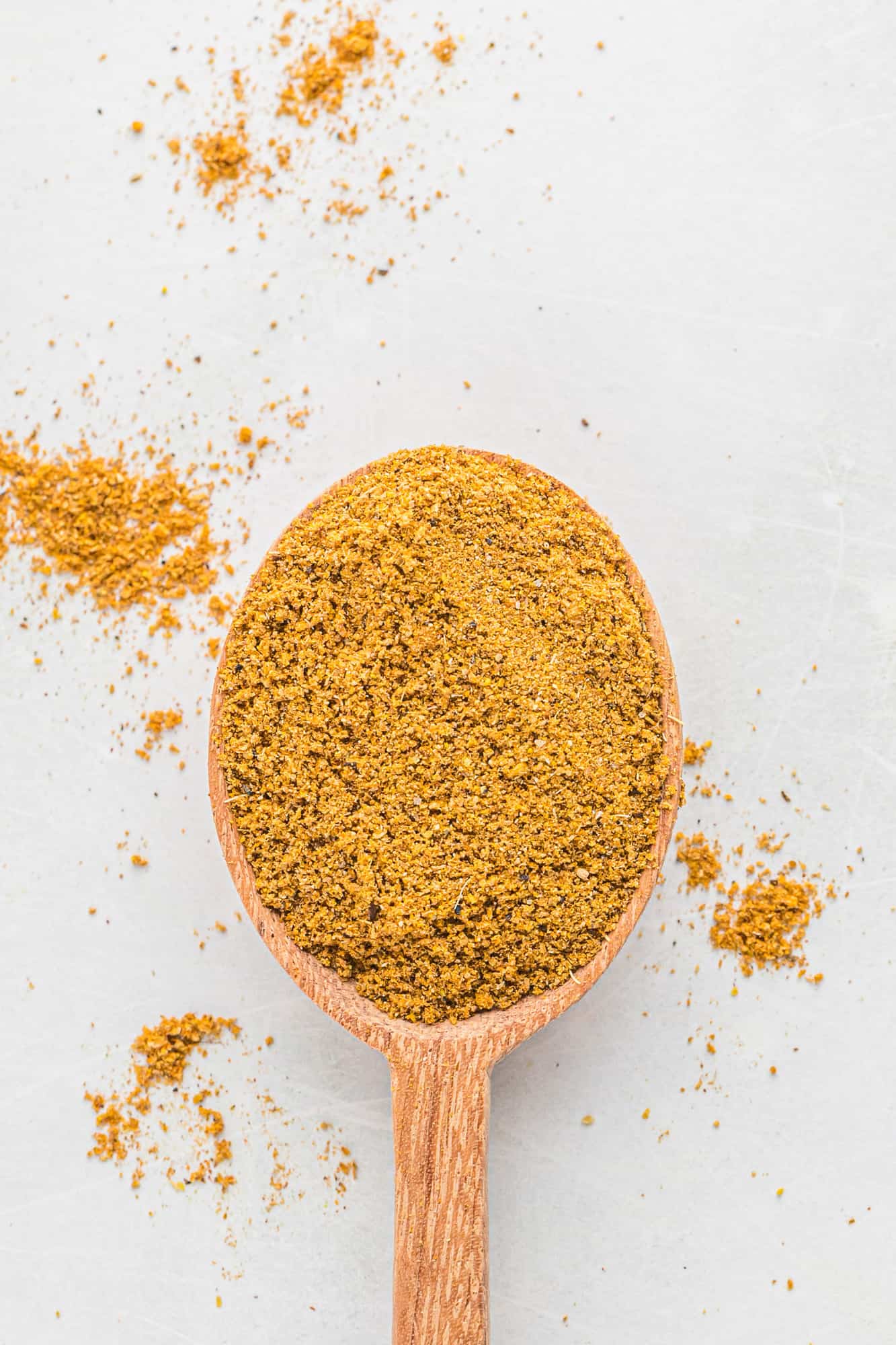 Curry powder on a wooden spoon on a white background.