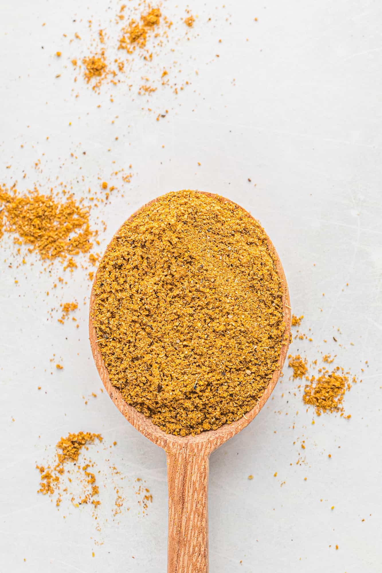 Curry powder on a wooden spoon on a white background.