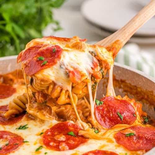 Pizza pasta being scooped from a pan with a wooden spoon.