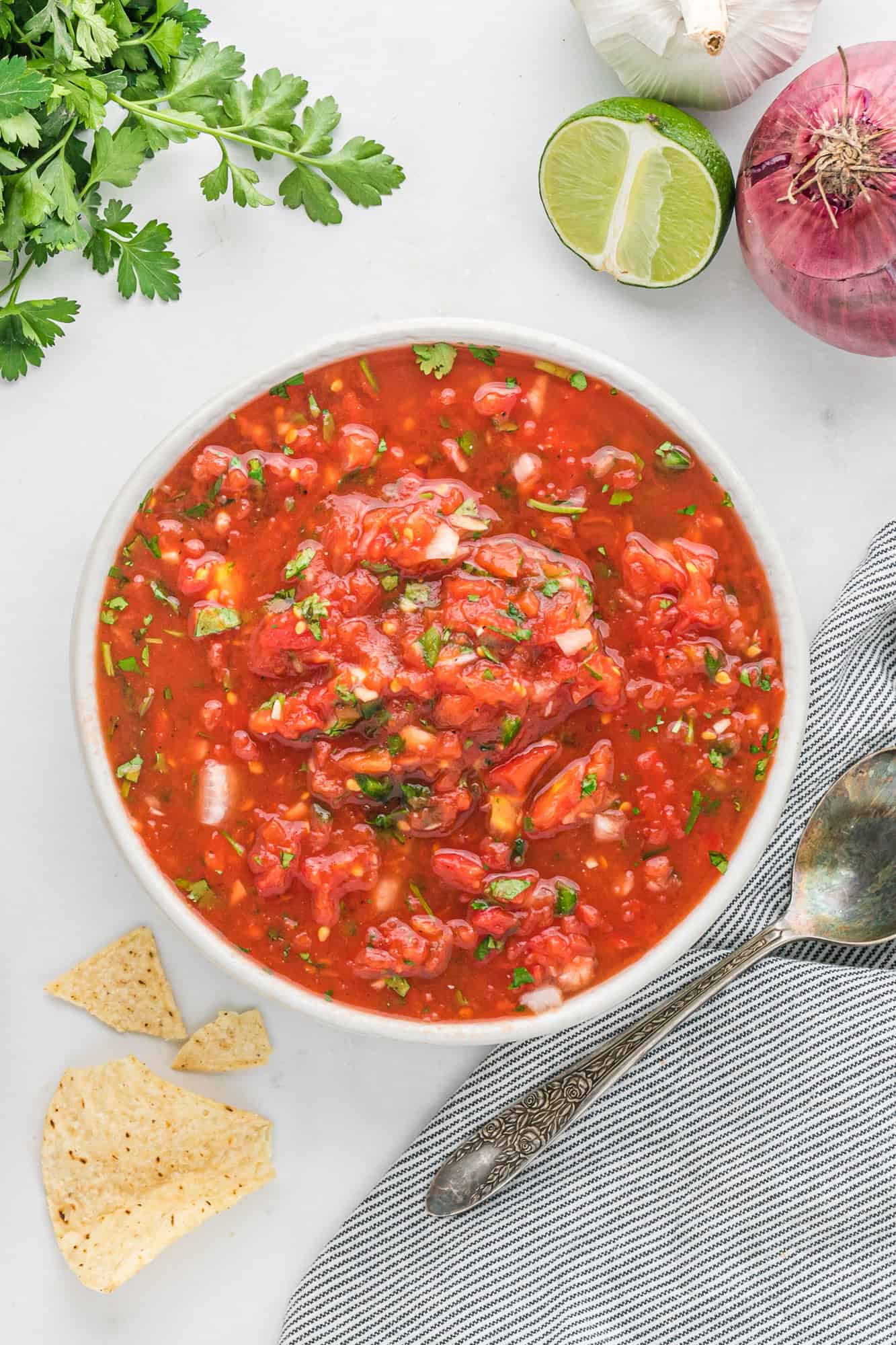 Bowl of homemade salsa surrounded by chips, cilantro, lime.