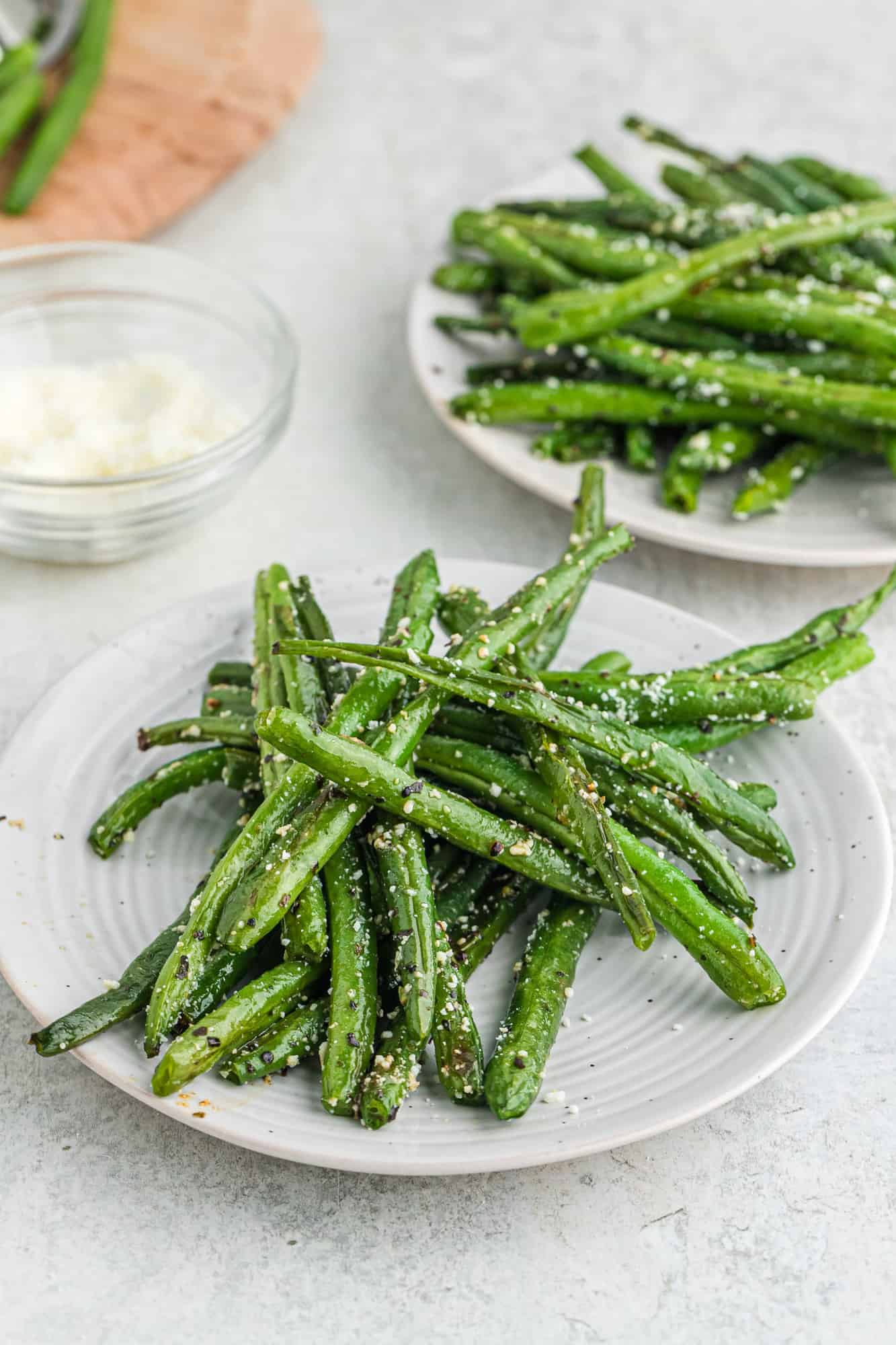Cooked green beans on two round white plates.