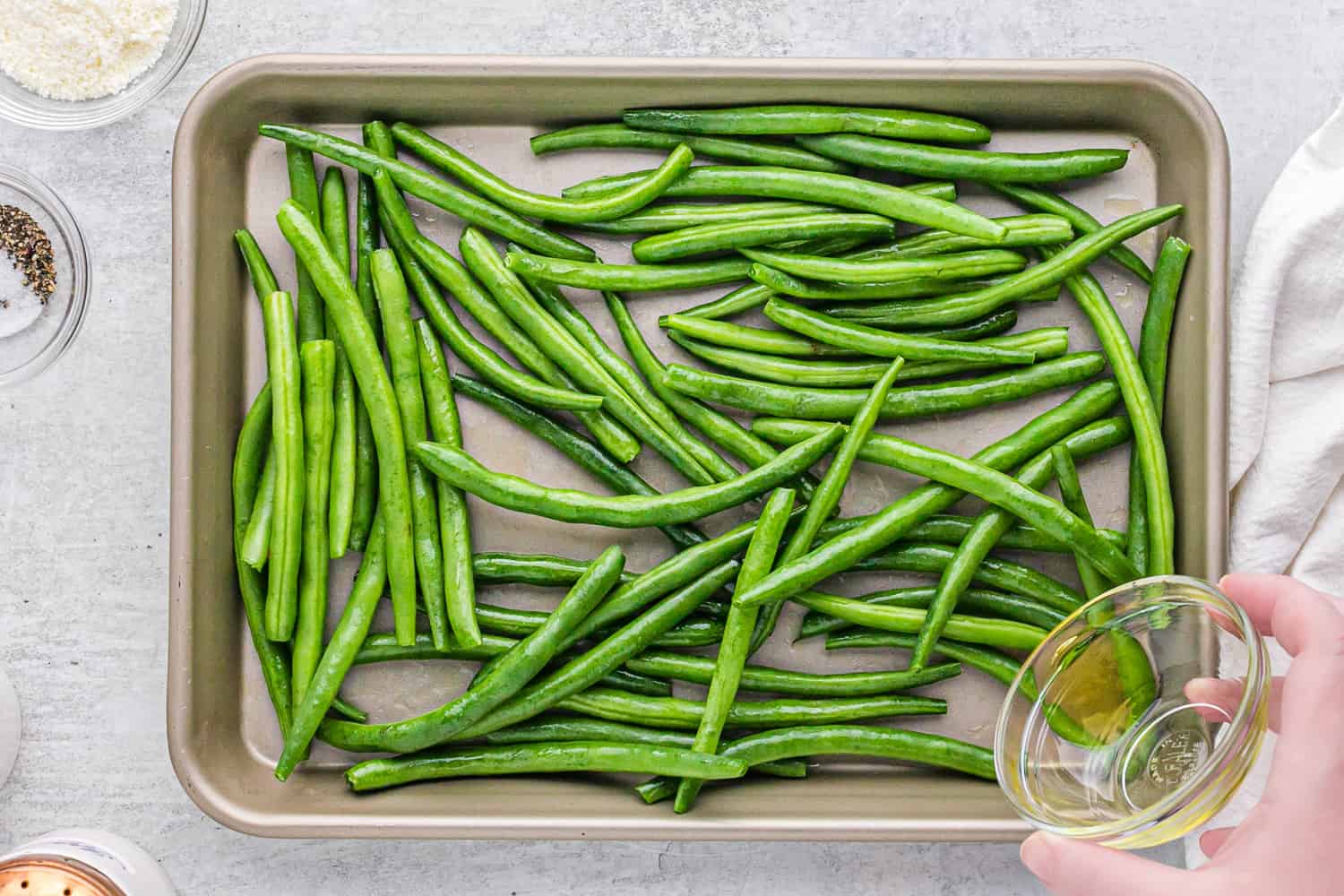 Green beans on a sheet pan with oil being added.