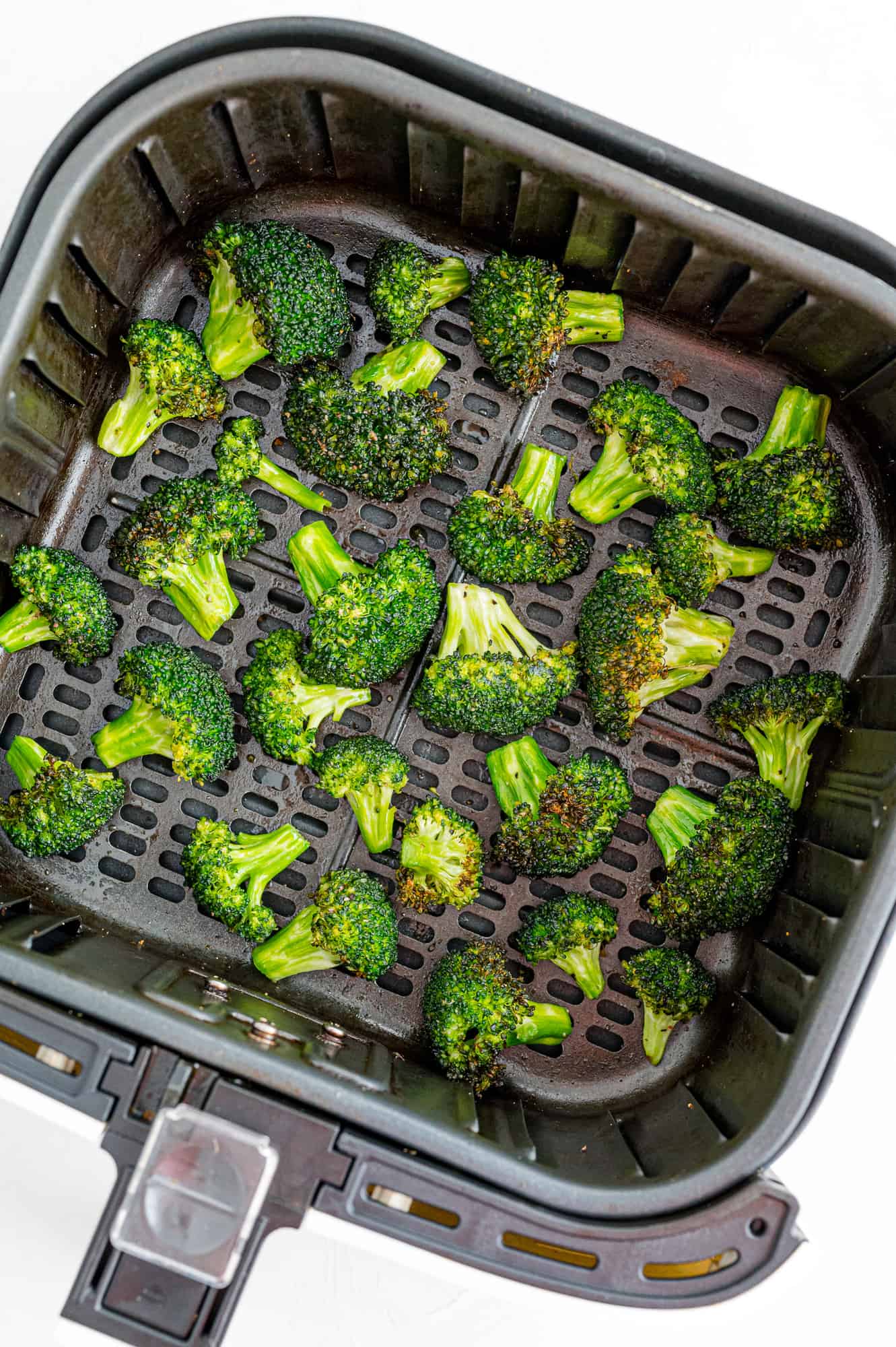 Cooked broccoli in an air fryer basket.