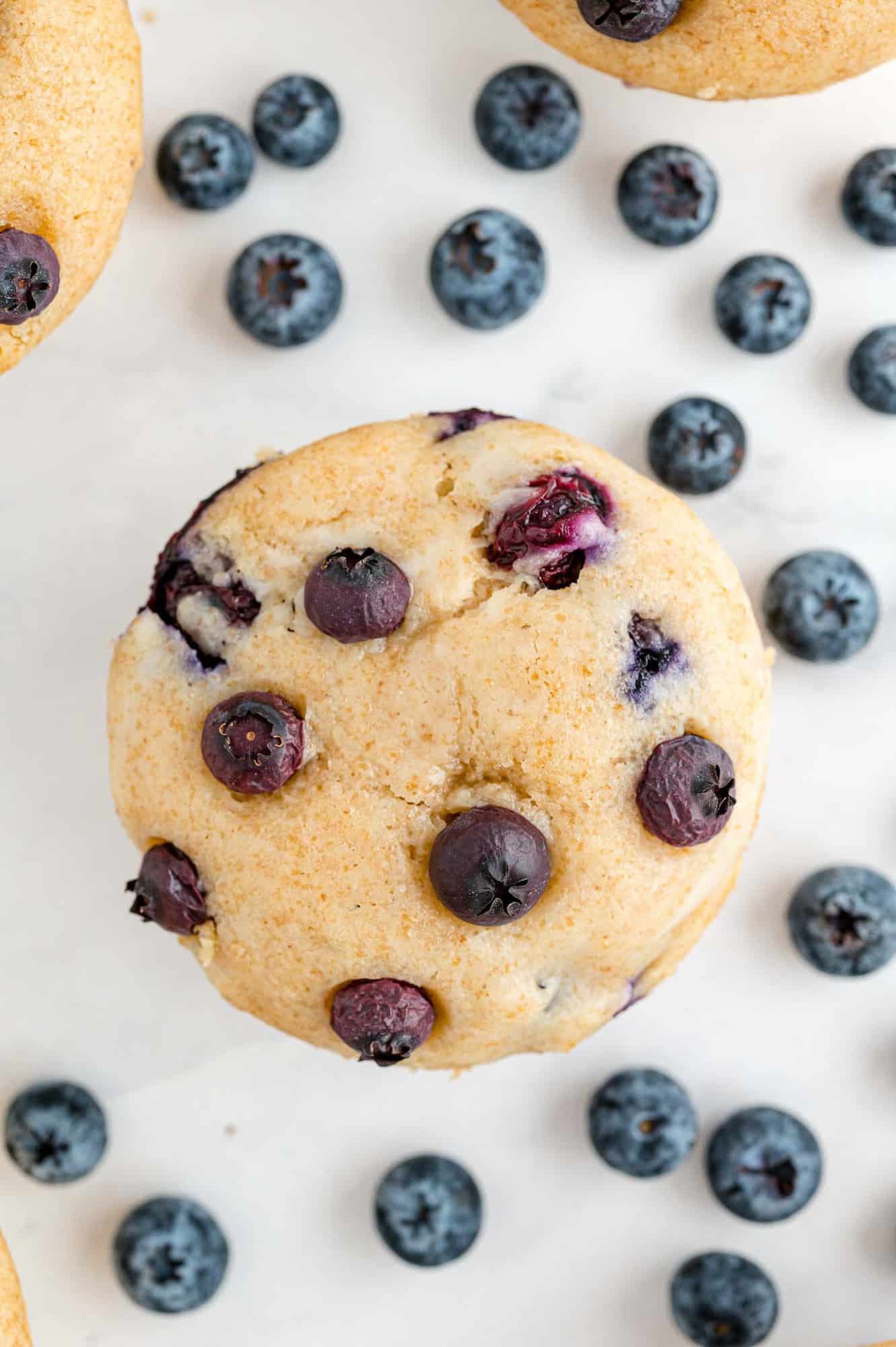 Overhead view of muffin with scattered fresh blueberries.