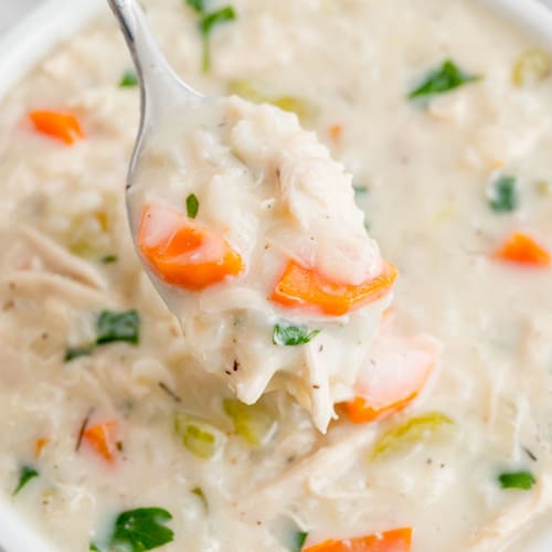 Spoonful of creamy chicken rice soup held over a bowl of soup.