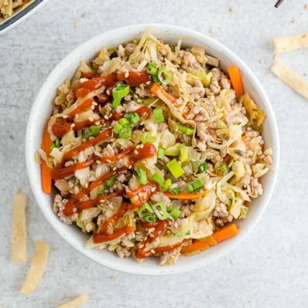 Overhead view of egg roll in a bowl drizzled with sriracha.