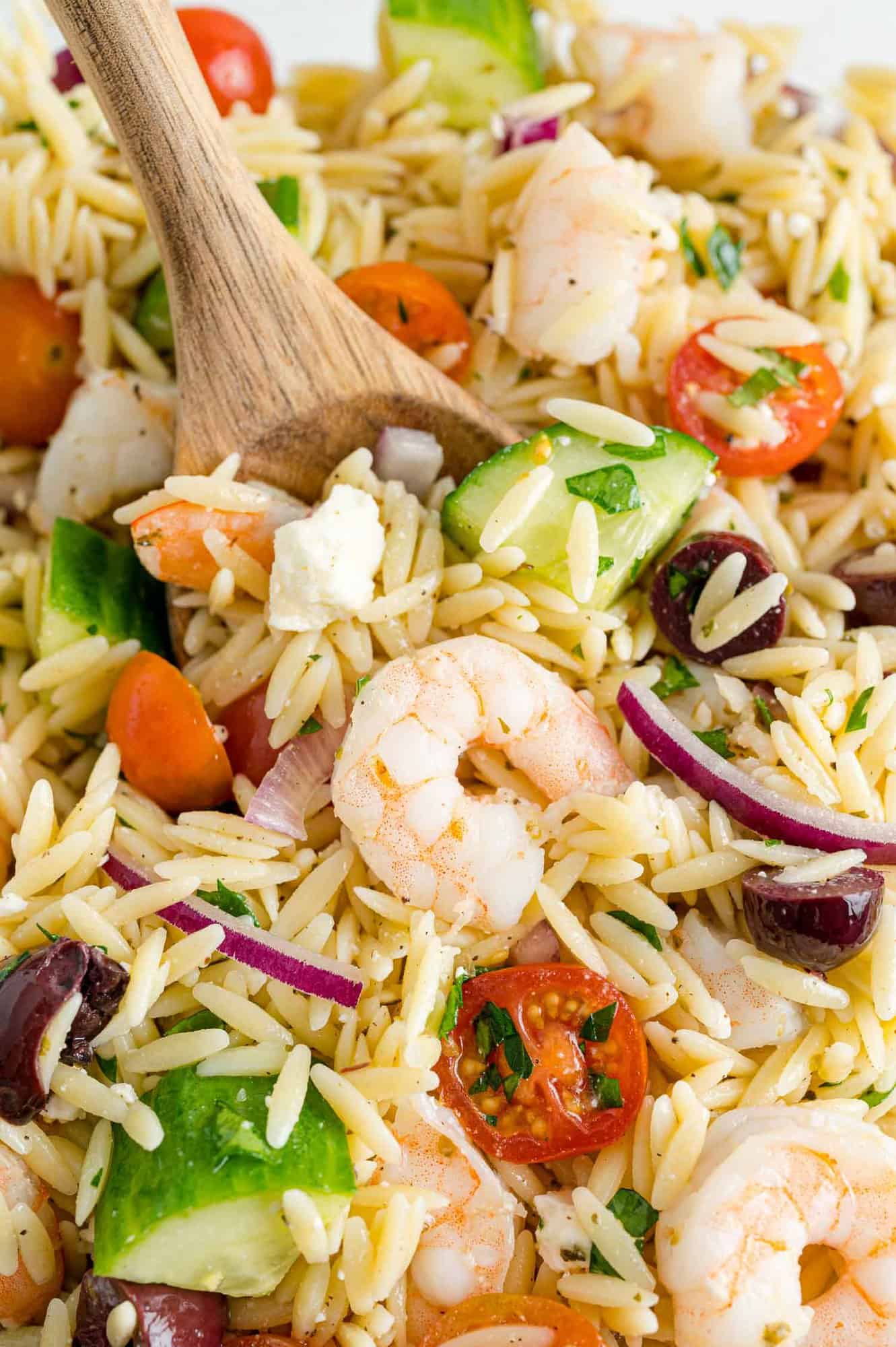 Close up of greek orzo salad with wooden spoon.