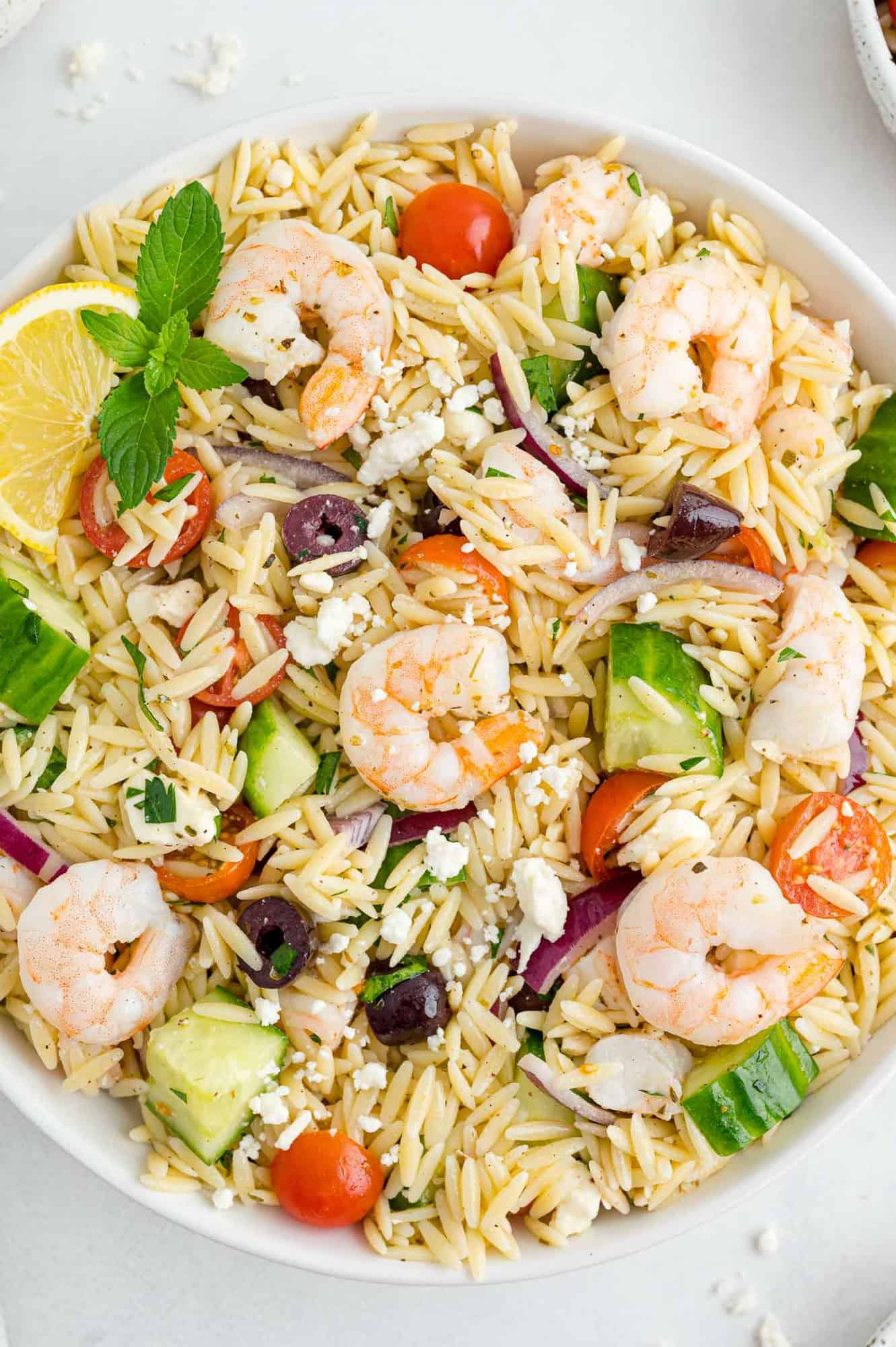 Large serving bowl of orzo salad with shrimp, olives, tomatoes, onions, feta, and more.