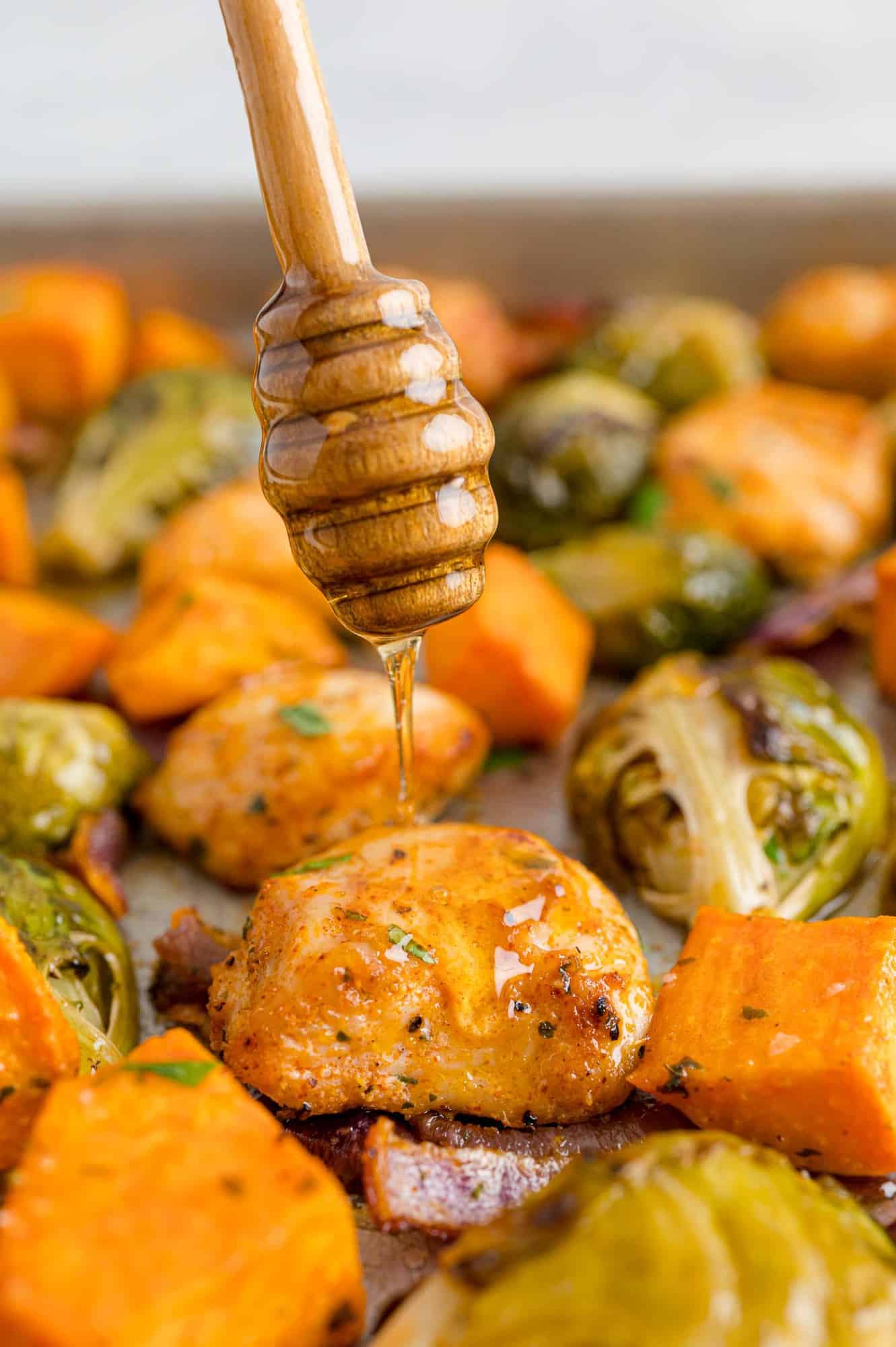 Sheet pan hot honey chicken with honey being added.