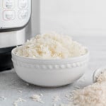 White rice in a white bowl with an instant pot in the background.