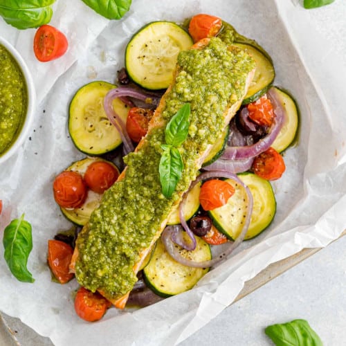 Vegetables and salmon topped with pesto in a parchment paper packet.