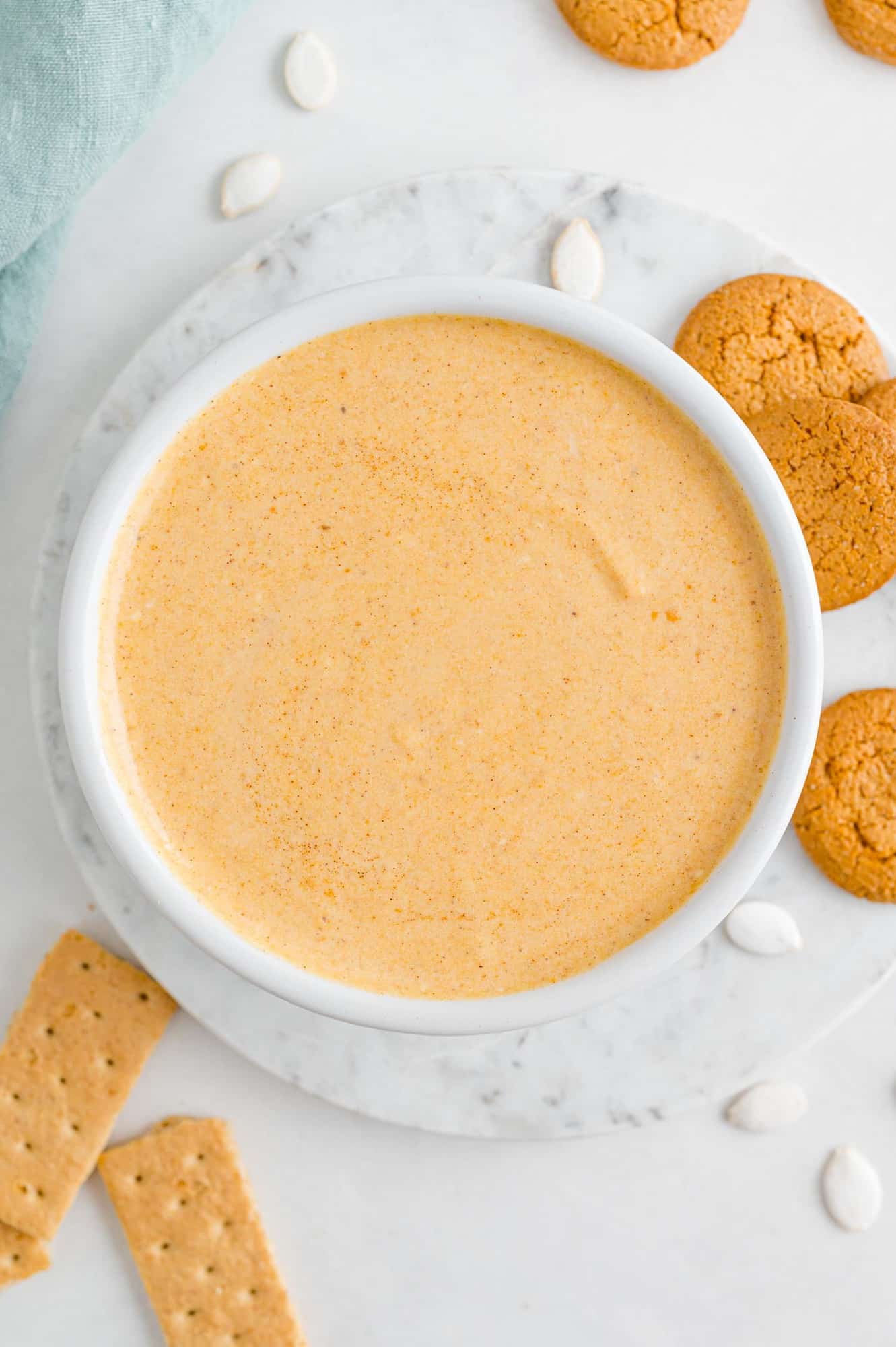 Overhead view of a bowl of pumpkin dip surrounded by gingersnap cookies and graham crackers.