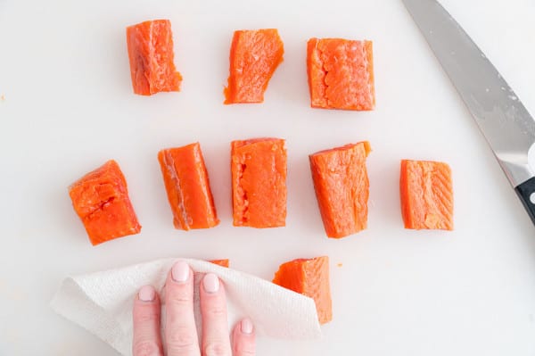 A hand patting salmon bites dry with a paper towel.