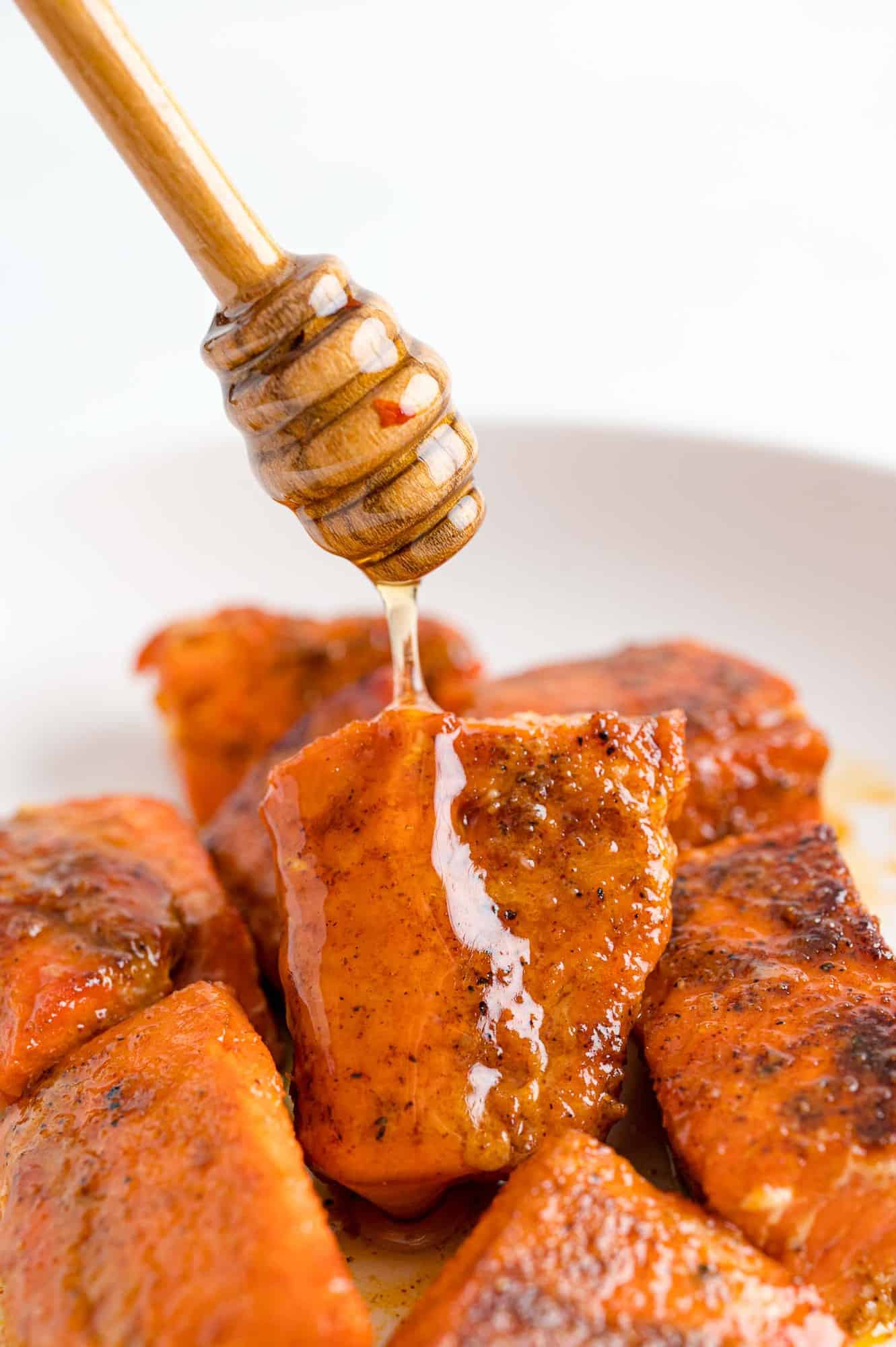 A honey wand drizzles hot honey over a bowl of salmon bites.