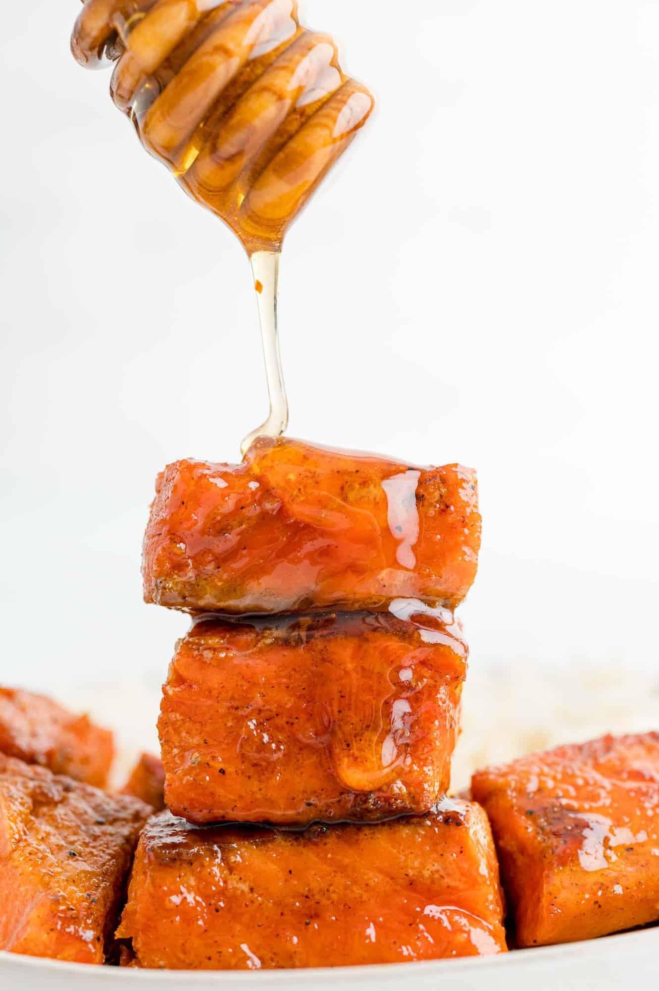 A stack of three salmon bites with hot honey being drizzled on from a honey wand.