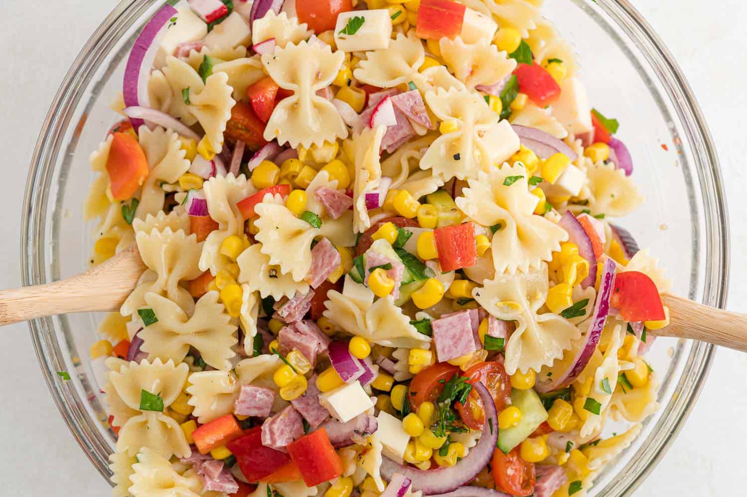 Summer pasta salad made with mini farfalle, being tossed.
