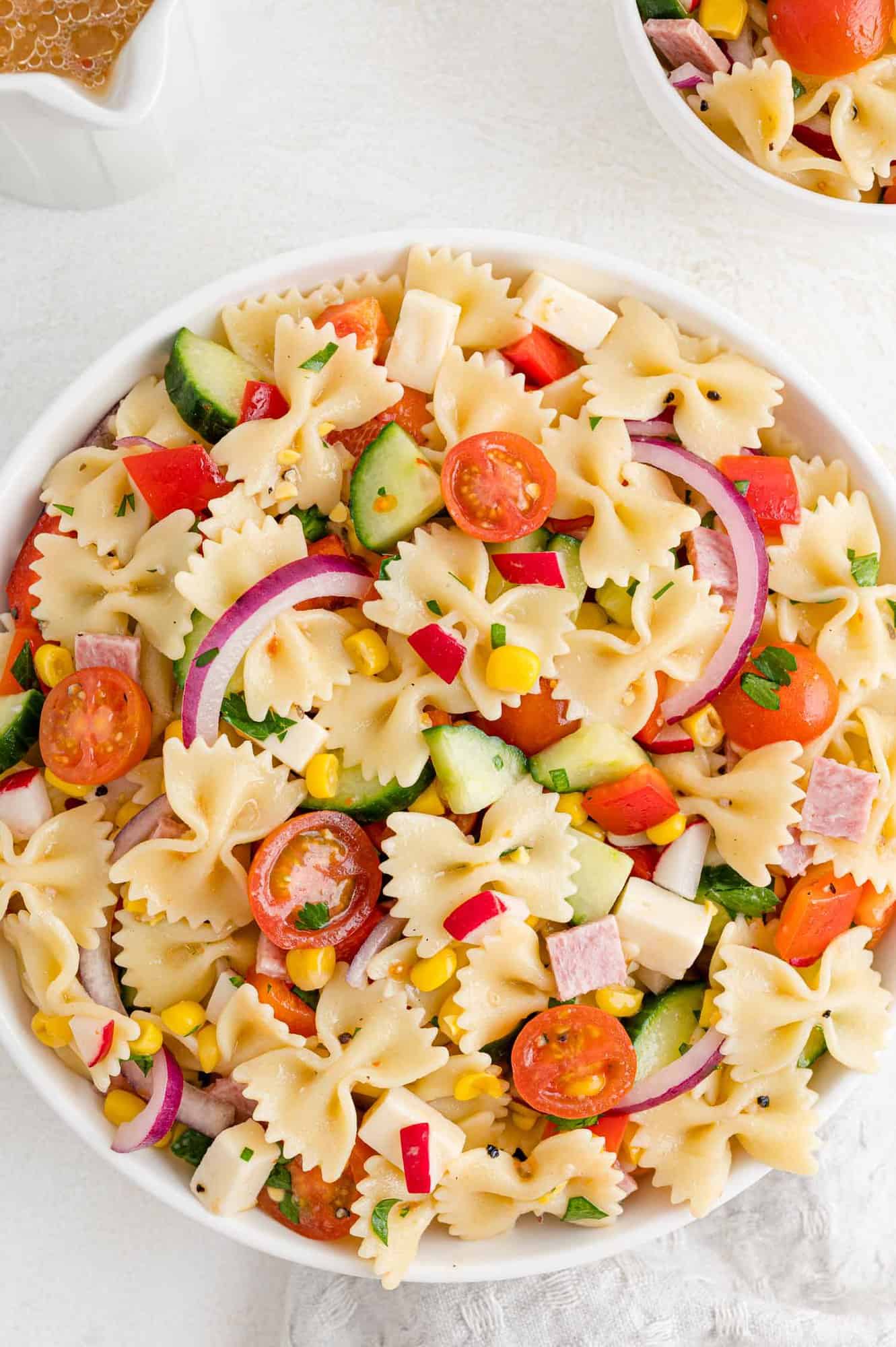 Summer pasta salad with bowtie pasta, in a round white bowl.