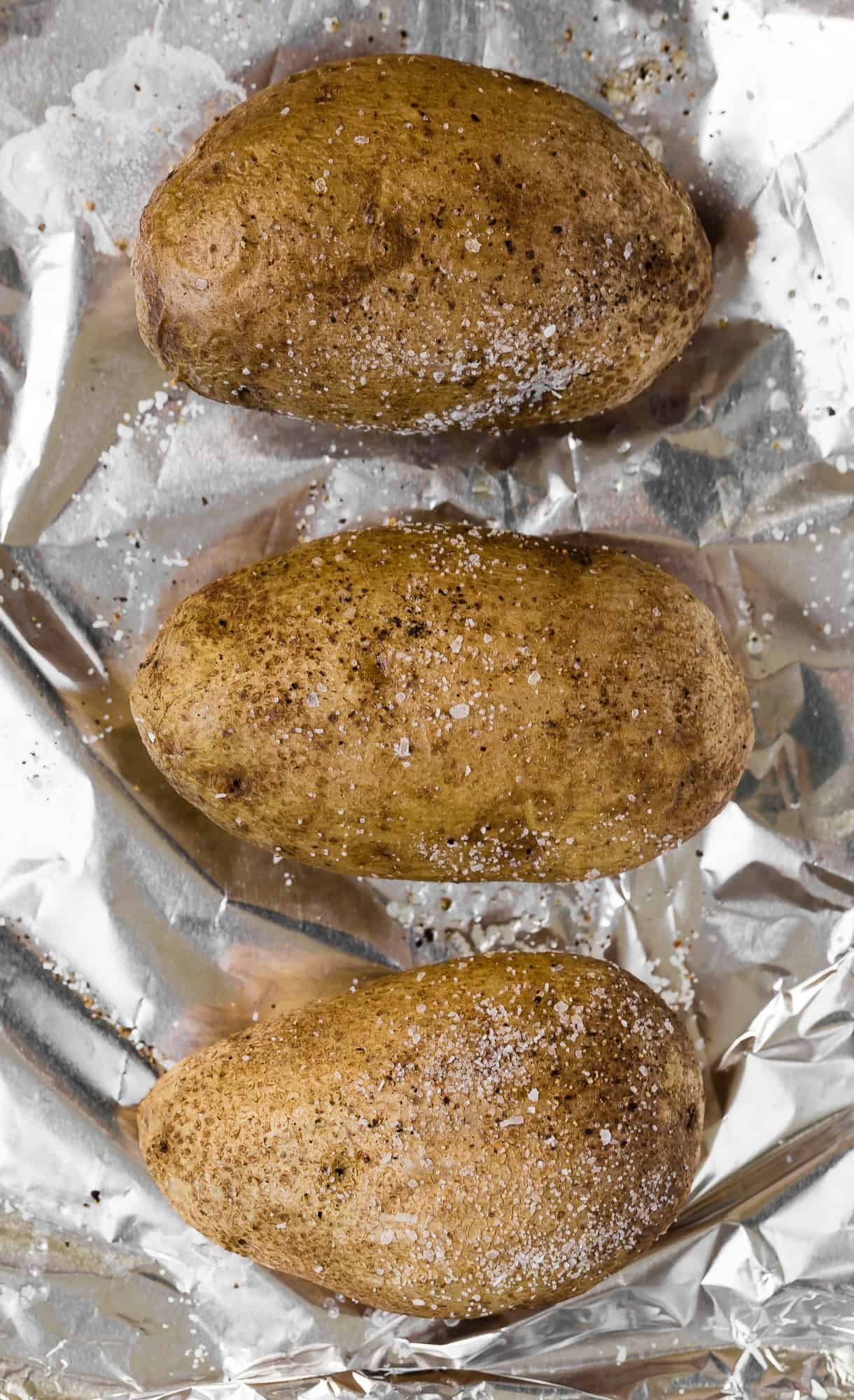 Three potatoes on a foil lined baking sheet.