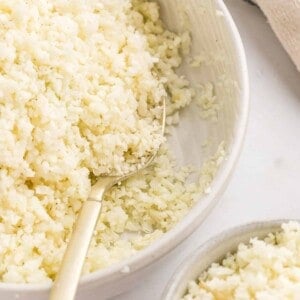Cauliflower rice in a bowl with a serving spoon.