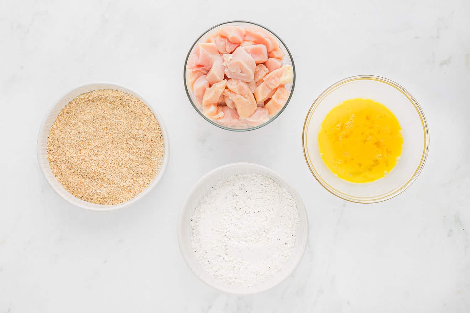 Four bowls, 3 with breading ingredients, one with chicken.