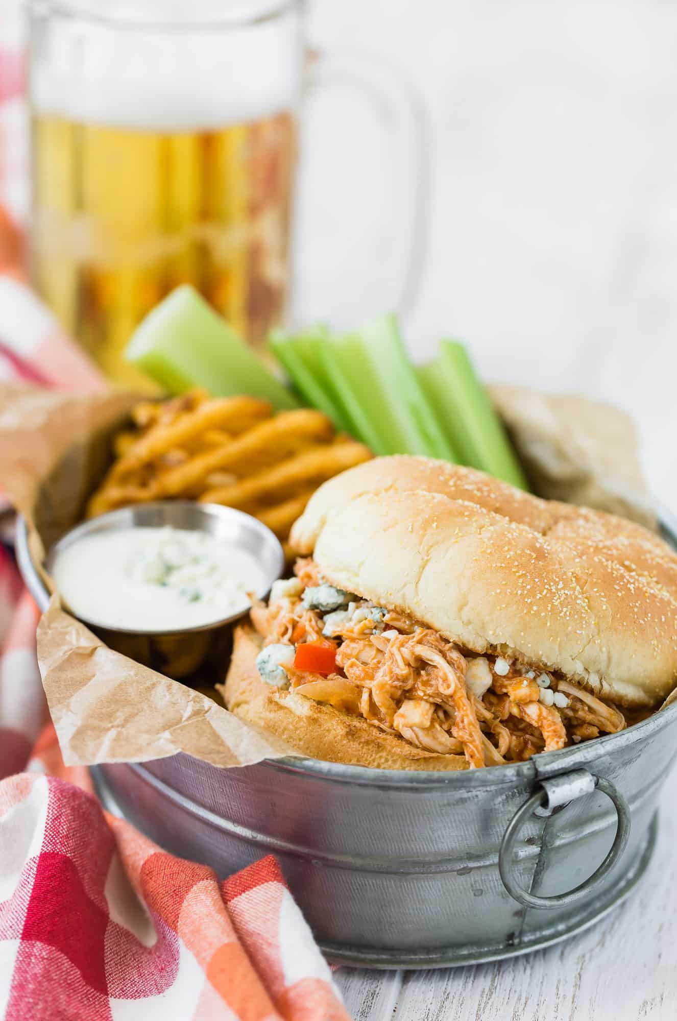 Buffalo chicken sandwich with beer in background.