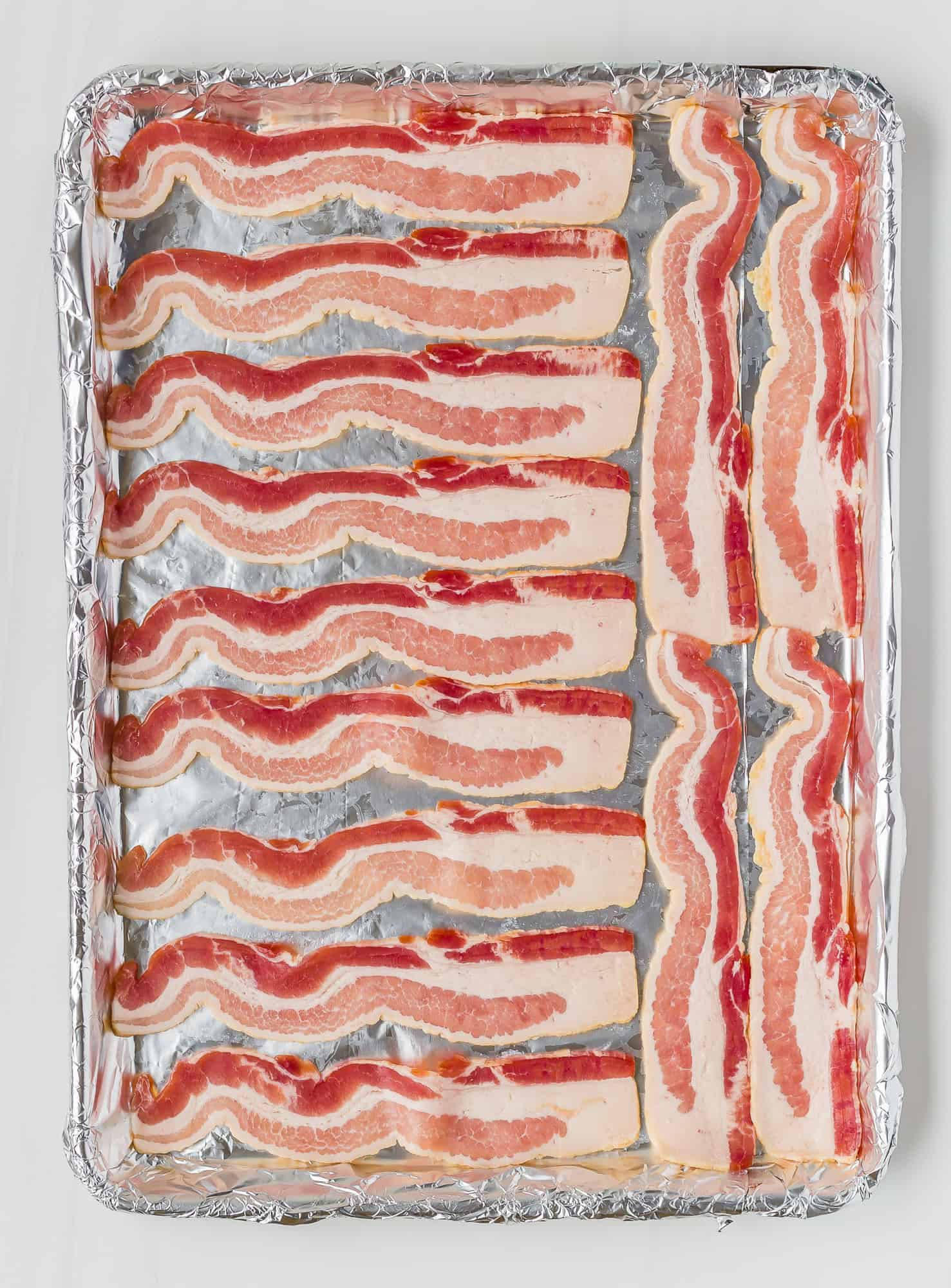 Uncooked bacon on a foil lined baking sheet.