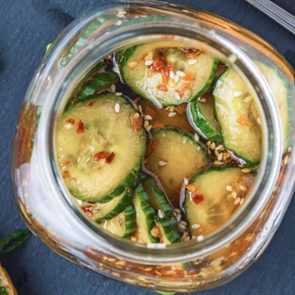 Korean pickles in a small glass jar, flecks of red pepper visible.