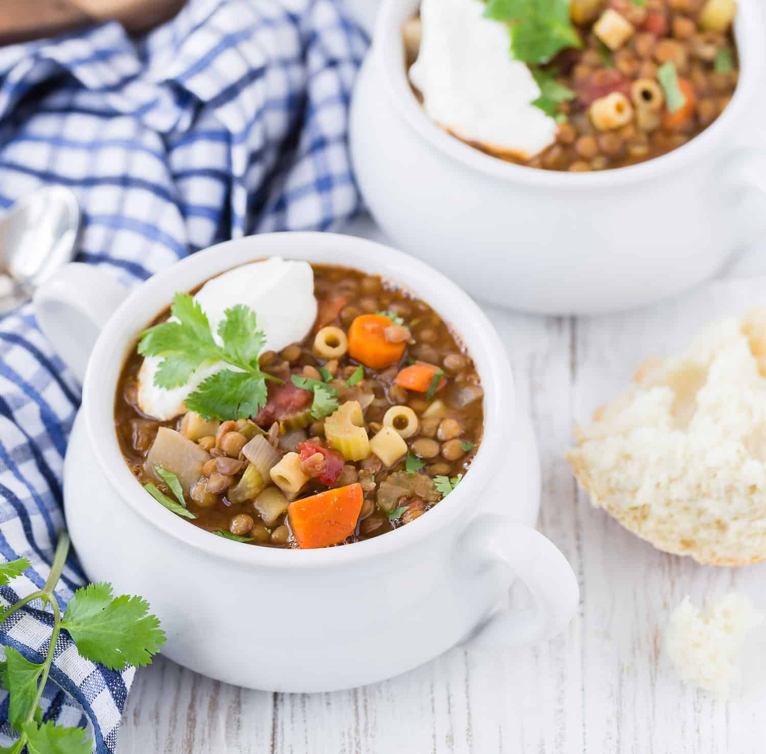 Image of two white bowls with handles, full of hearty lentil soup. Each bowl is topped with a dollop of greek yogurt and fresh cilantro leaves.