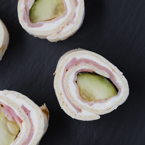 Pickle roll ups with ham on a black background.