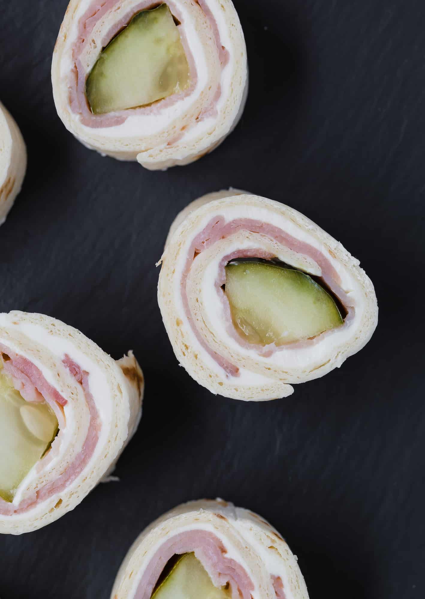 Pickle and ham roll ups in slices on a black background.