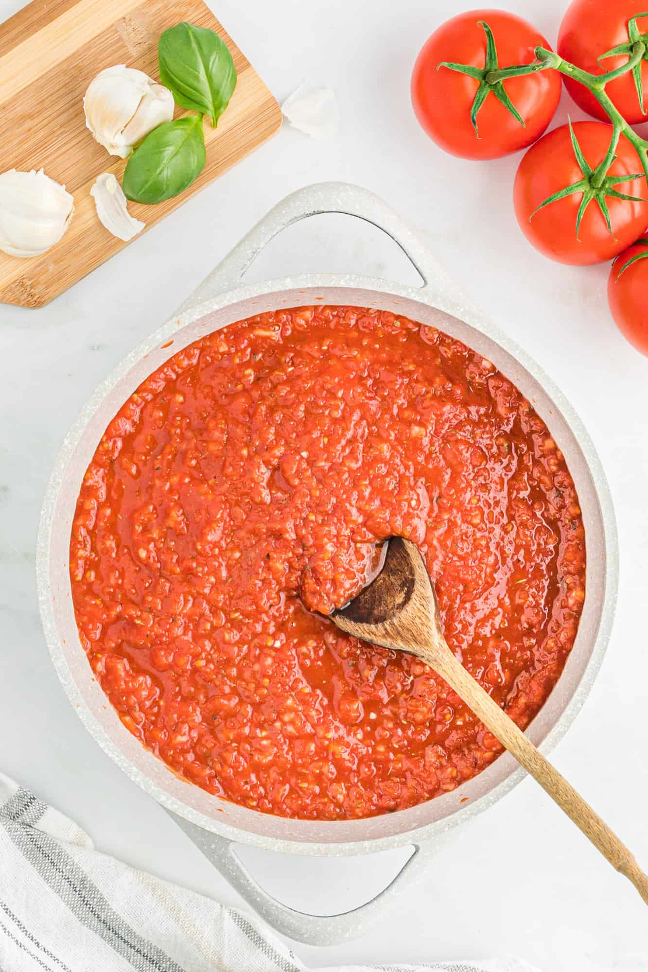 Pizza sauce in a large white pan with a wooden spoon.