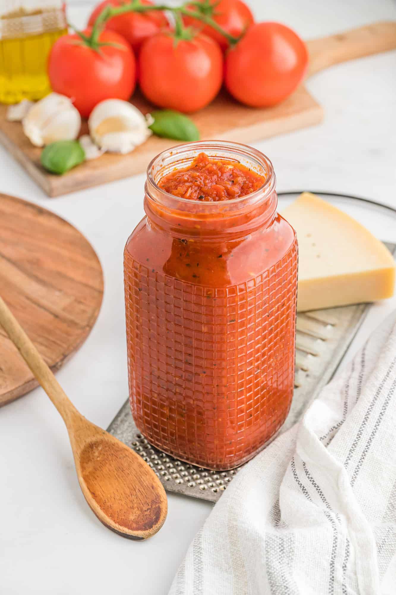 Homemade pizza sauce in a glass jar with tomatoes in the background.