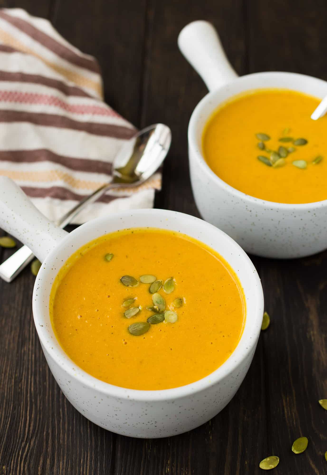 Two bowls of pumpkin curry soup with pepitas.