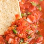 Close up of restaurant style salsa with a chip being dipped in.