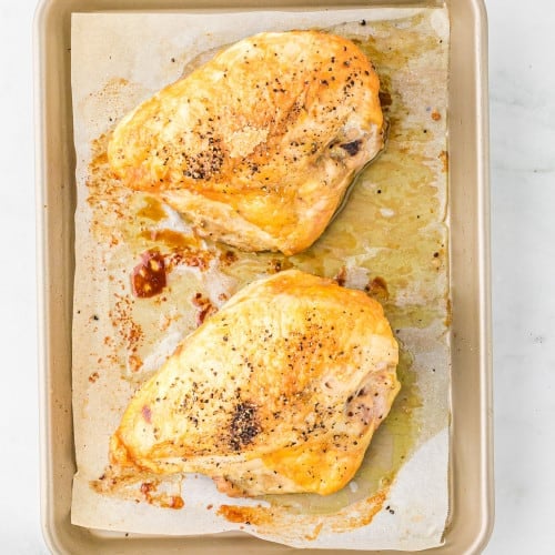 Two roasted chicken breasts on a sheet pan.