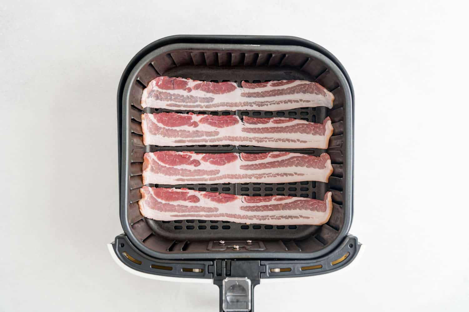 Uncooked bacon in air fryer basket.