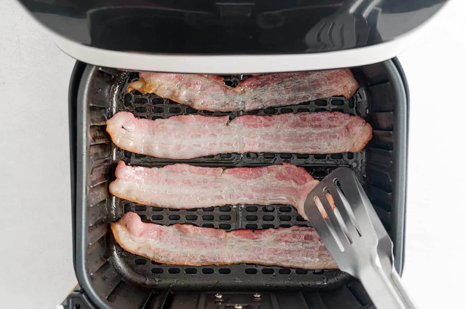 Bacon in air fryer being flipped.