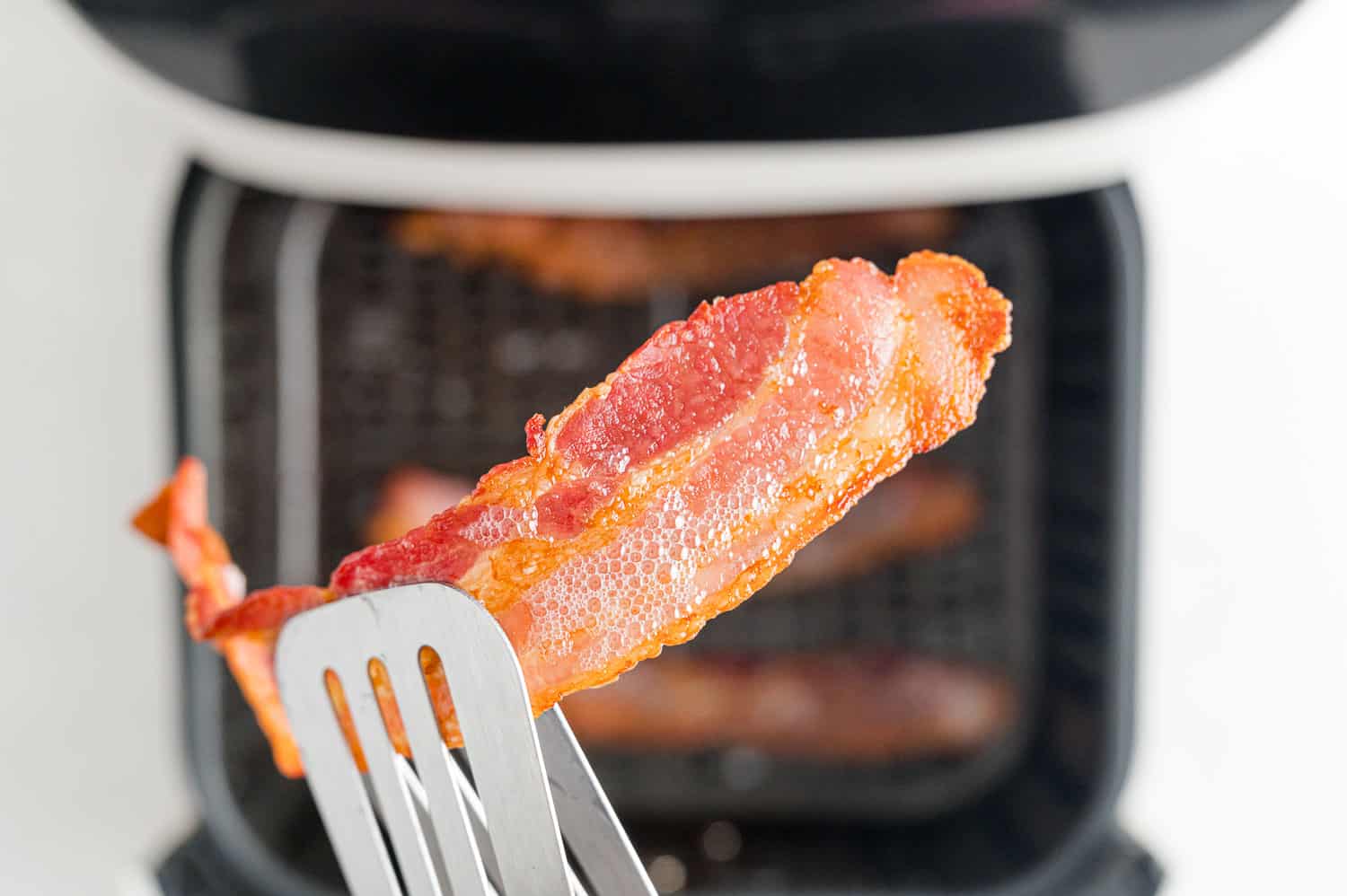 Cooked bacon held with tongs.