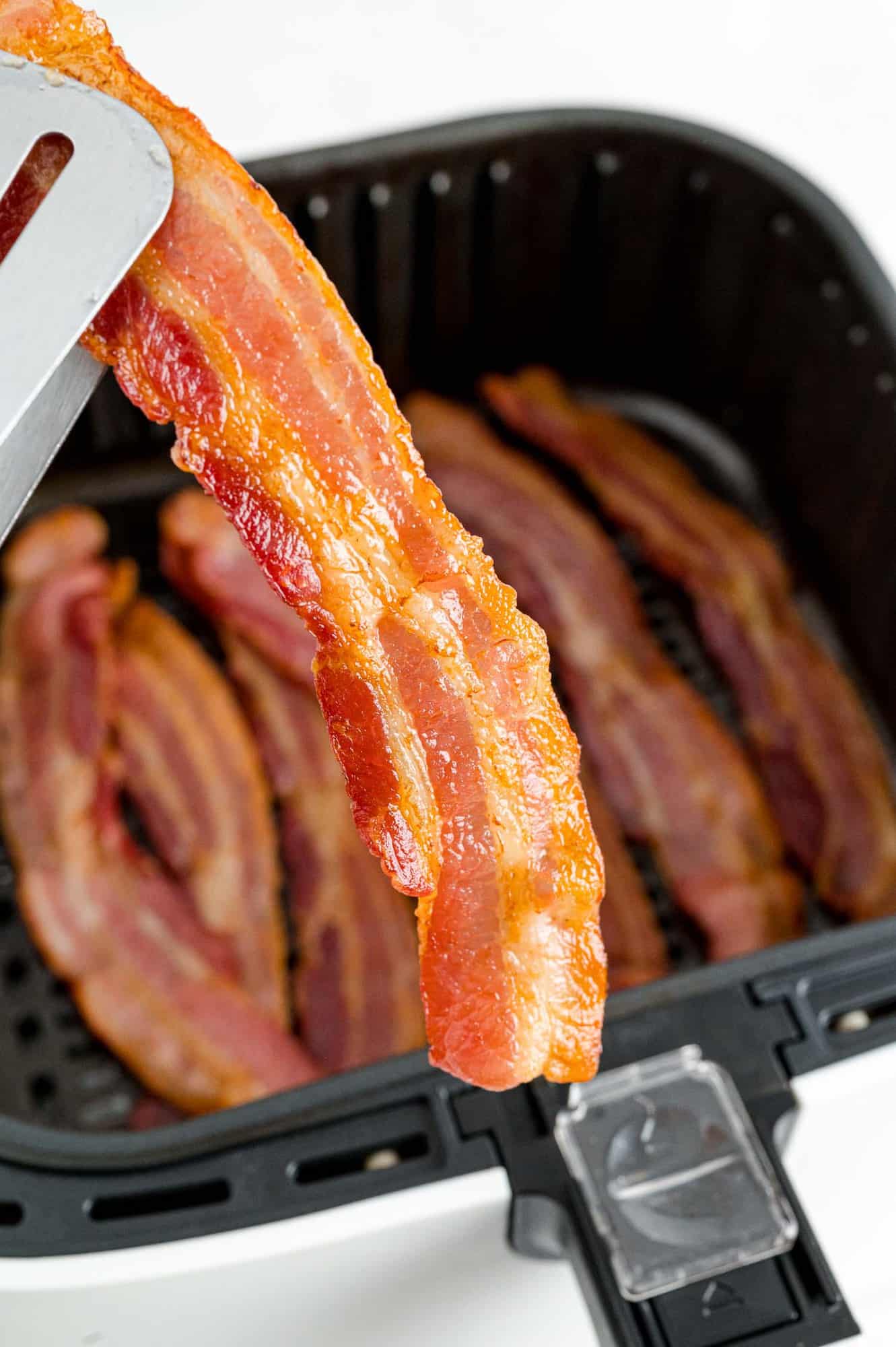Cooked bacon being taken out of an air fryer.
