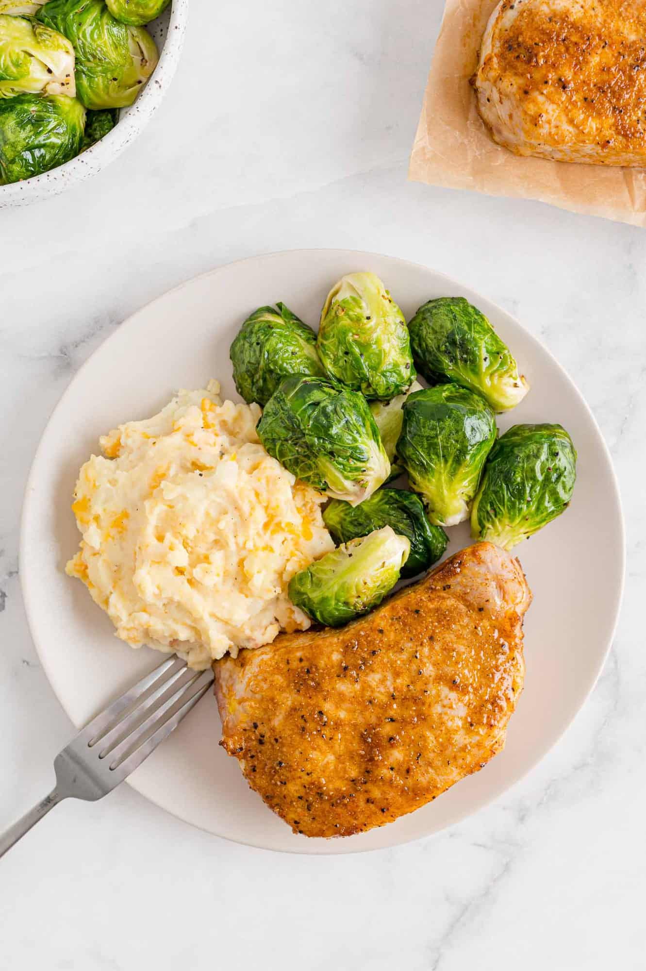 Pork on a plate with potatoes and brussels sprouts.