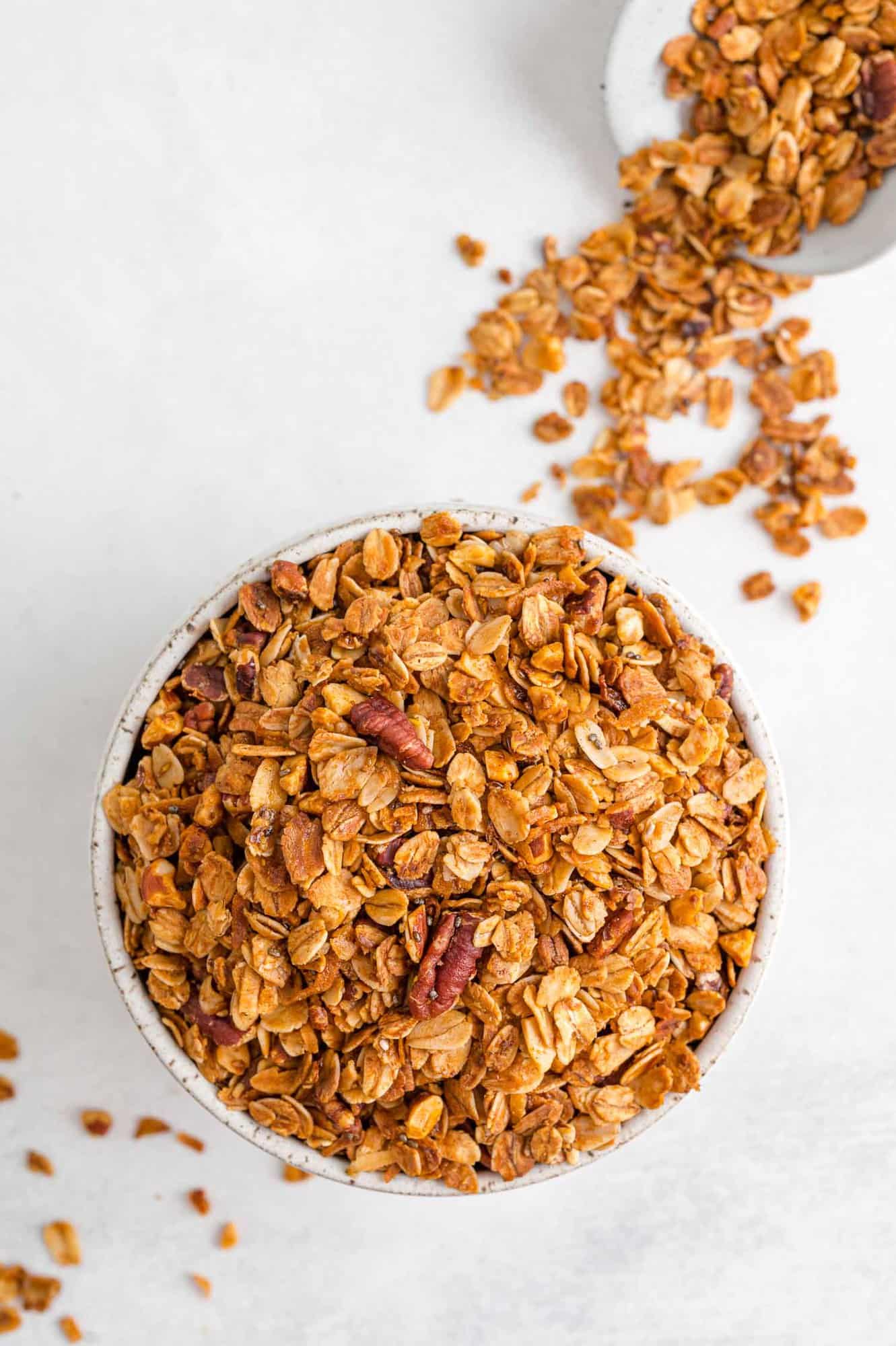 Granola in a bowl with more on white surface.