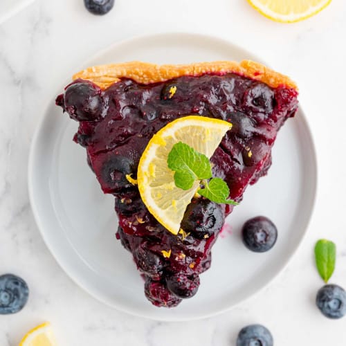 Overhead view of fresh blueberry pie on a white plate.