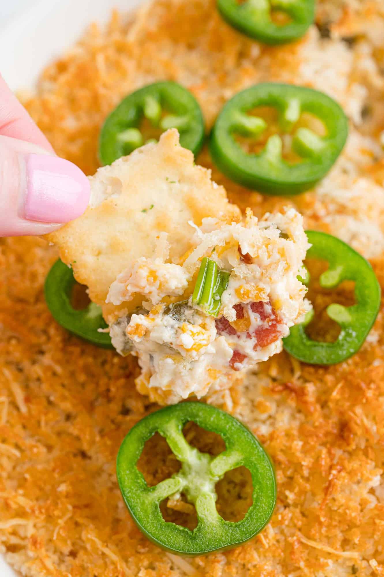 Jalapeño popper dip on a cracker and in baking dish.