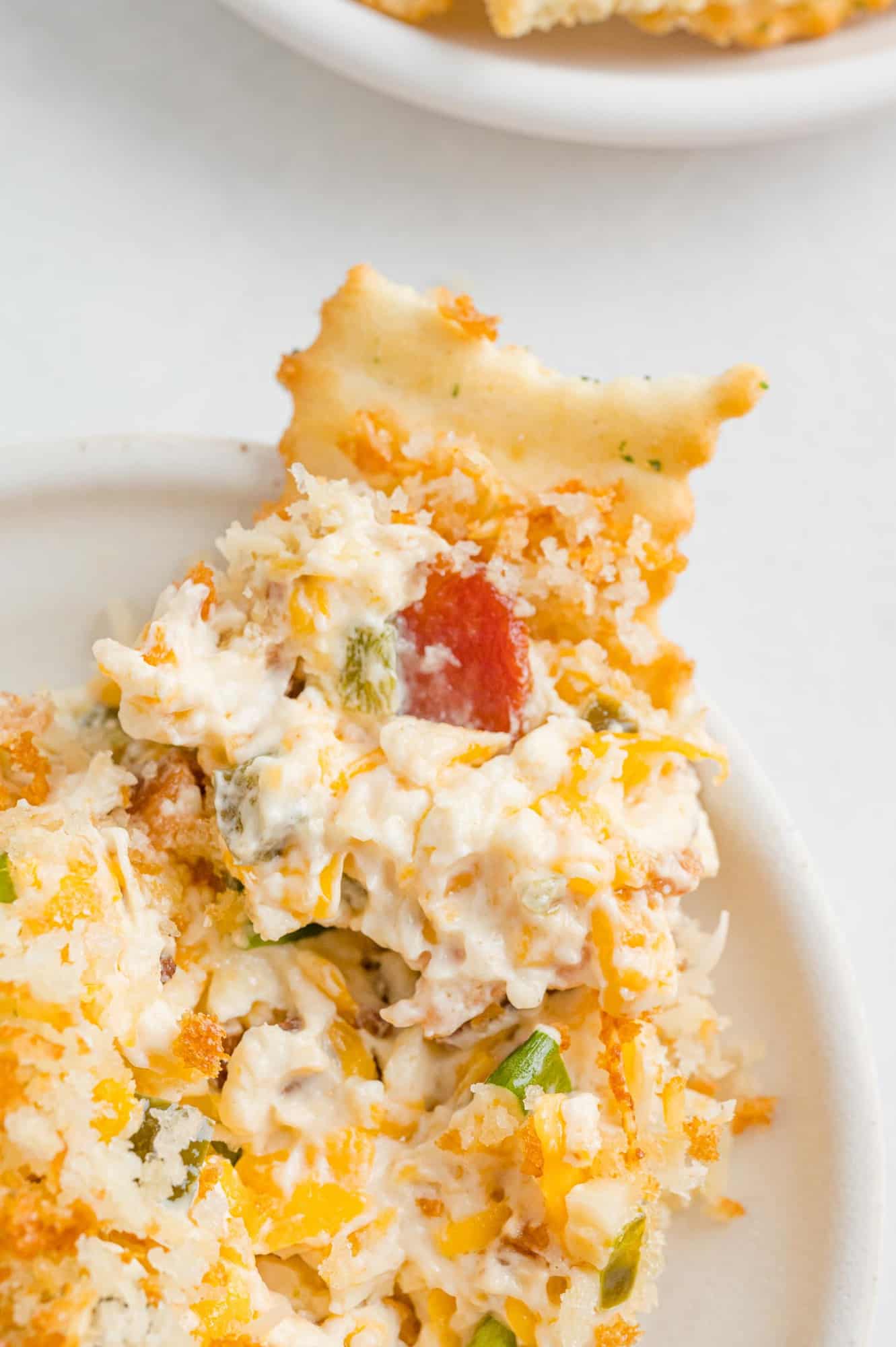 Pile of cheesy dip with jalapeño and bacon, a cracker dipped in.